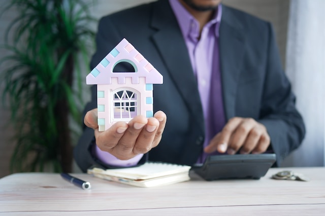 man holding small house with calculator